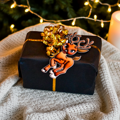 Reinsdyr til og fra lapp til julegavene som festes i gavebåndet rundt julegaven. Gavelappen er i boble effekt og skiller seg ut fra vanlige gavelapper. Man får følelsen av en 3d effekt. Her ligger gaven på et teppe med juletreet i bakgrunnen. Skriv hvem gaven er til og fra på baksiden av lappen. 