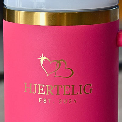 Rosa hjertelig termokopp med gullkant- nærbilde av logoen og gullkanten. Nydelige lasergraverte hjerter over logoen som gir den et luksuriøst preg. Gulldetaljene gjør dette til en drikkeflaske du kommer til å få komplimenter for. Perfekt gave til noen som ikke får i seg nok drikke. 