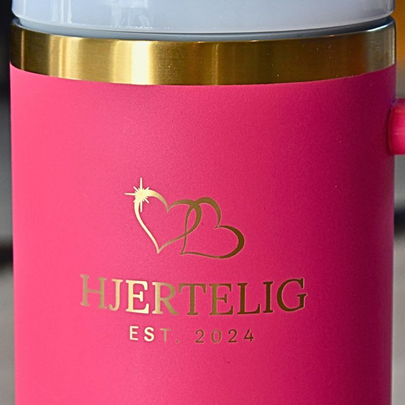 Rosa hjertelig termokopp med gullkant- nærbilde av logoen og gullkanten. Nydelige lasergraverte hjerter over logoen som gir den et luksuriøst preg. Gulldetaljene gjør dette til en drikkeflaske du kommer til å få komplimenter for. Perfekt gave til noen som ikke får i seg nok drikke. 