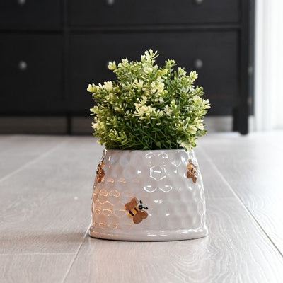 En blomsterpotte med grønn plante. Potten er designet som en bikube med søte bier. Nydelig detalje til ditt hjem. Fyll den med dine favoritt blomster og gi hjemmet ditt en nydelig detalj. 
