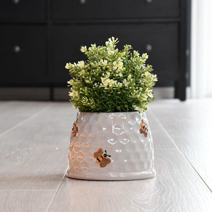 En blomsterpotte med grønn plante. Potten er designet som en bikube med søte bier.