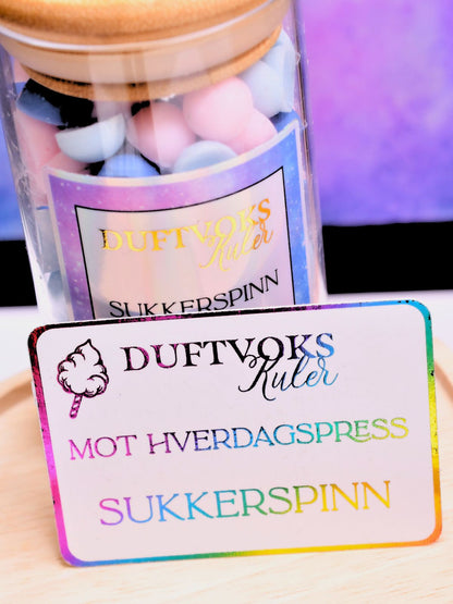 Kortet som følger med denne duftvoksen har reinbuens farger. På dette fine kortet står det at disse duftvokskulene er mot hverdagspress og lukter sukkerspinn. Et søtt kort som følger med glasset. 