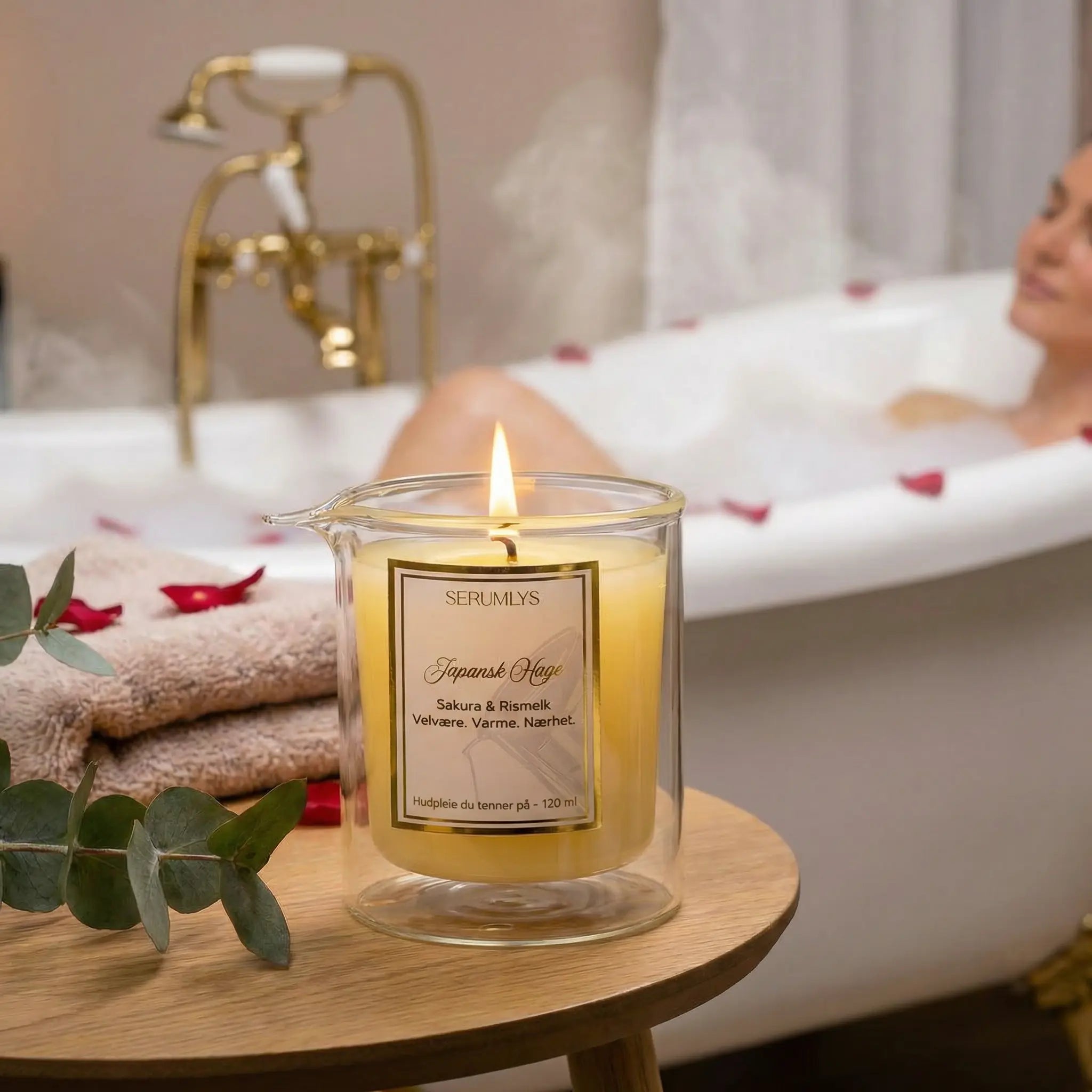 Et serumlys med duft av sakura og rismelk som står plassert på et bord. Et lys som er laget med naturlige planteoljer. Et hudpleieprodukt som kan brukes på hele kroppen. En dame ligger og slapper av i badekaret mens lyset står tent. Etter 15-20 minutter har noe av bivoksen smeltet, og serumet er klar til bruk. Varm og behagelig olje som tilfører fuktighet og glød. Varmen er beroligende og kan bidra til å redusere stress. En liten spabehandling hjemme på eget bad.