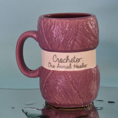 Hekle krus med teksten Crocheter - one armed hooker. Koppen ser ut som et garn nøste med merkelapp på, og er en fin gave til jul eller bursdag til alle som elsker å hekle.