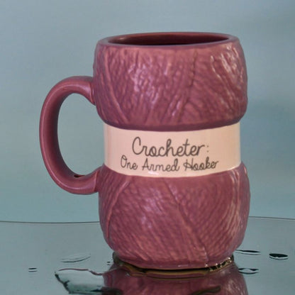 Hekle krus med teksten Crocheter - one armed hooker. Koppen ser ut som et garn nøste med merkelapp på, og er en fin gave til jul eller bursdag til alle som elsker å hekle.