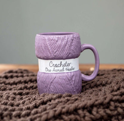 Lilla kaffekopp formet som garn. Koppen er i lilla farge med en humoristisk tekst Crocheter One armed hooker. En gøy gave å gi til alle som elsker å hekle. 