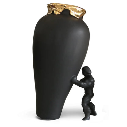 En superhelt som støtter en sort vase som ser ut til å falle. Vasen er i sort farge og har en gullkant. Superhelten er i sort og samme farge som vasen. Et kunstverk som håndlages i nederland.