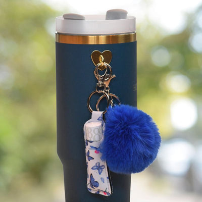 Blå veske med sommerfugl motiv som henger på en termokopp. Denne vesken er til liptick, så har du den alltid med deg uansett hvor du er!