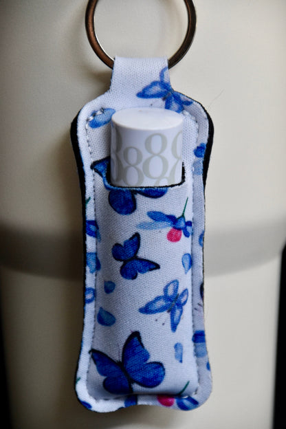 en veske til lipsyl eller leppepomade med sommerfugl motiv som er festet på en beige termokopp. Kan også festes på sekker, nøkkelringer, jakke osv. Lipsyl eller leppestilt lett tilgjengelig. 