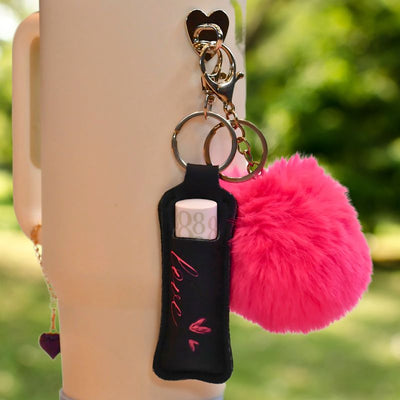 Lipstick veske svart med rosa skrift hvor det står love. Her henger den på en termokopp ute. 