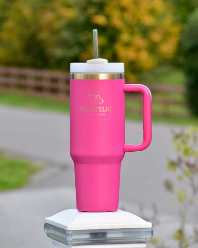 Tumbler med sugerør og håndtak i rosa farge med gullkant og logo. Her står den ute og man ser de nydelige gulldetaljene som lasergravert hjertelig logo og med gull hjerter over. En nydelig drikkeflaske som garantert vil komme godt med. Varm eller kald drikke hele dagen! Praktisk og luksuriøst utsende. 