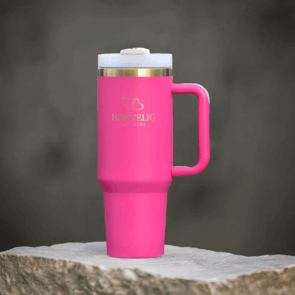 Rosa Hjertelig termokopp med gullkant og gull-logo utstilt på en stein. Eksklusiv drikkeflaske som holder drikken din varm eller kald i mange timer. Perfekt når man er på farten, så vil man alltid ha favoritt drikken sin lett tilgjengelig. 