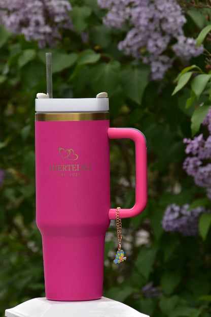 Et smykke med sommerfugl motiv som viser hvordan det ser ut når den er festet på en rosa termokopp med sugerør og håndtak med gullkant
