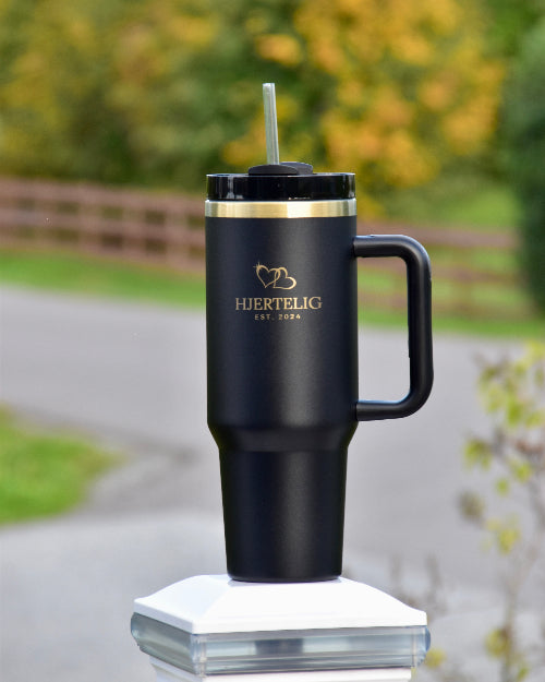 Tumbler med sugerør i sort farge med gullkant og logo. Gulldetaljene gir termokoppet et luksuriøst preg og den passer perfekt i de fleste koppholderene i bilen, noe som gjør den lett å ta med seg ut når man er på farten. Lasergravert logo og hjerter på koppen. 
