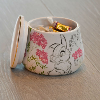 En krukke med lokk fra Disney med Trampe motiv. Rosa detaljer og gullkantpå lokket. Krukken er fylt opp med karameller. Lokket er tatt av og står ved siden av krukken.