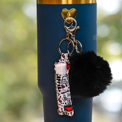 Veske til lipstick med kaffemotiv som henger på termokopp med gullkant.