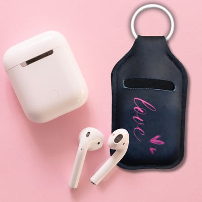 En nøkkelring med en liten sort veske med rosa love tekst som brukes til å oppbevare airpods.