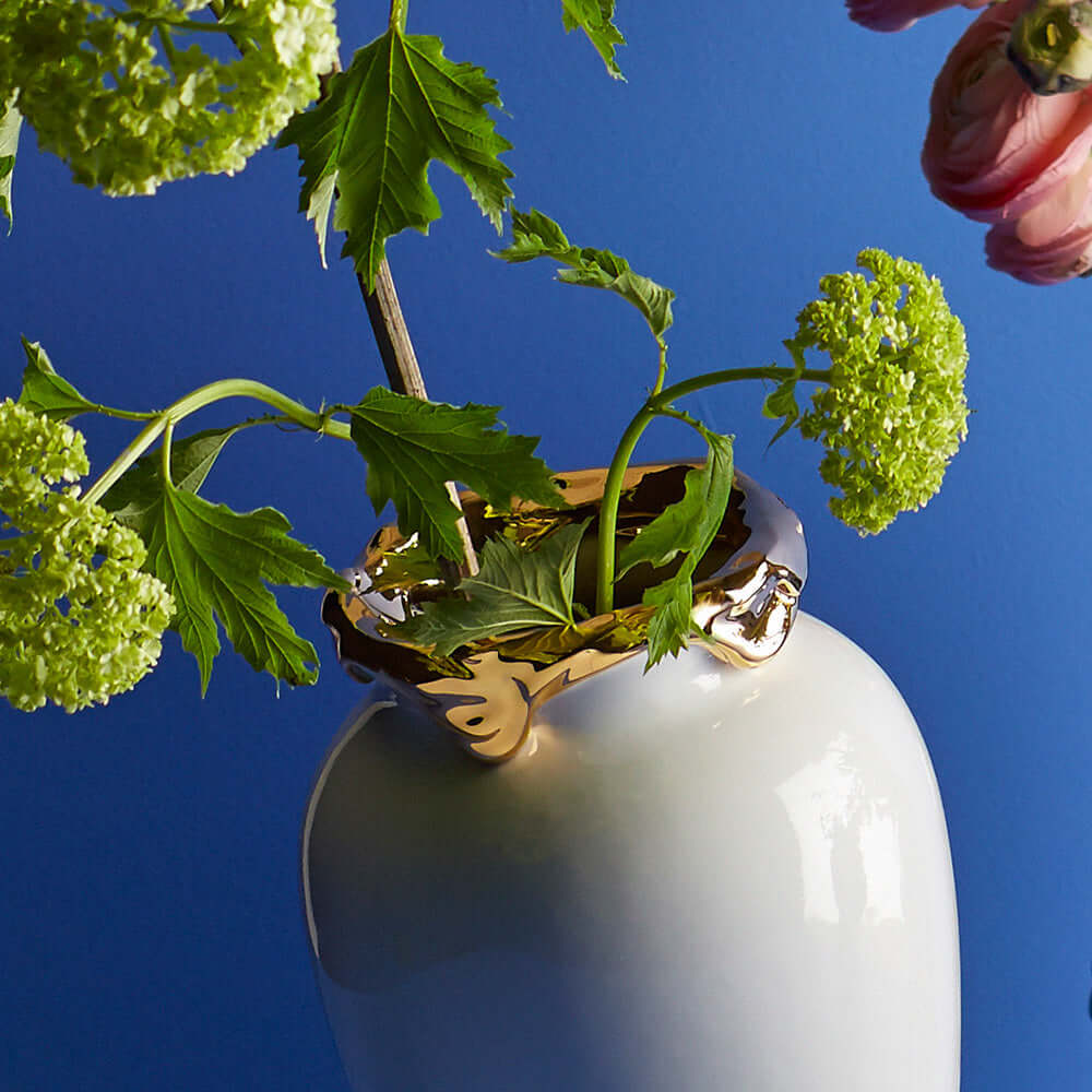 Et nærbilde av en hvit vase med gullkant med grønne blomster