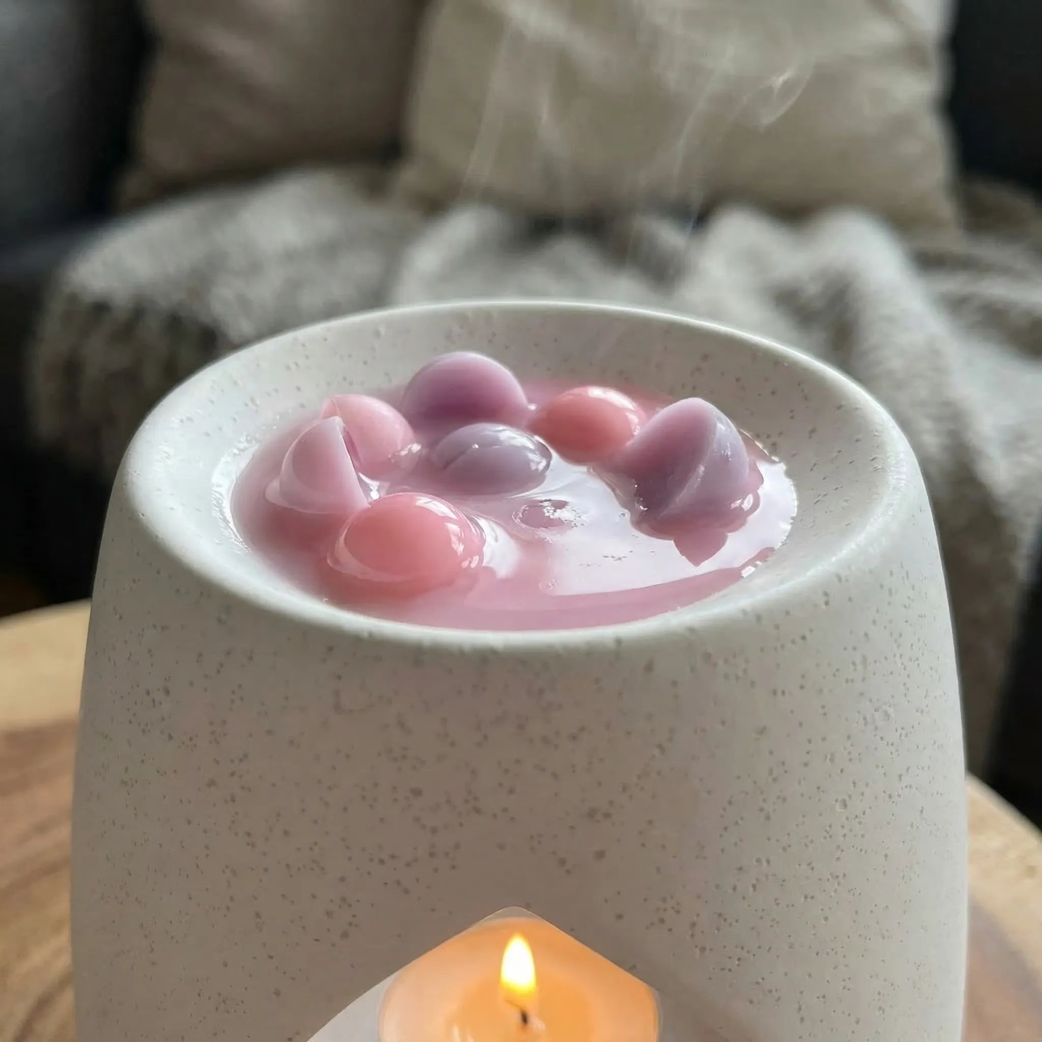 En duftbrenner som smelter noen vokskuler med duft av nyvasket tøy. Små rosa og lilla vokskuler, håndlaget i Norge med bivoks og soyavoks. Bivoksen hjelper til med å øke smeltetiden og varigheten på duften. Voksen kan også brukes flere ganger før den byttes ut med en ny.