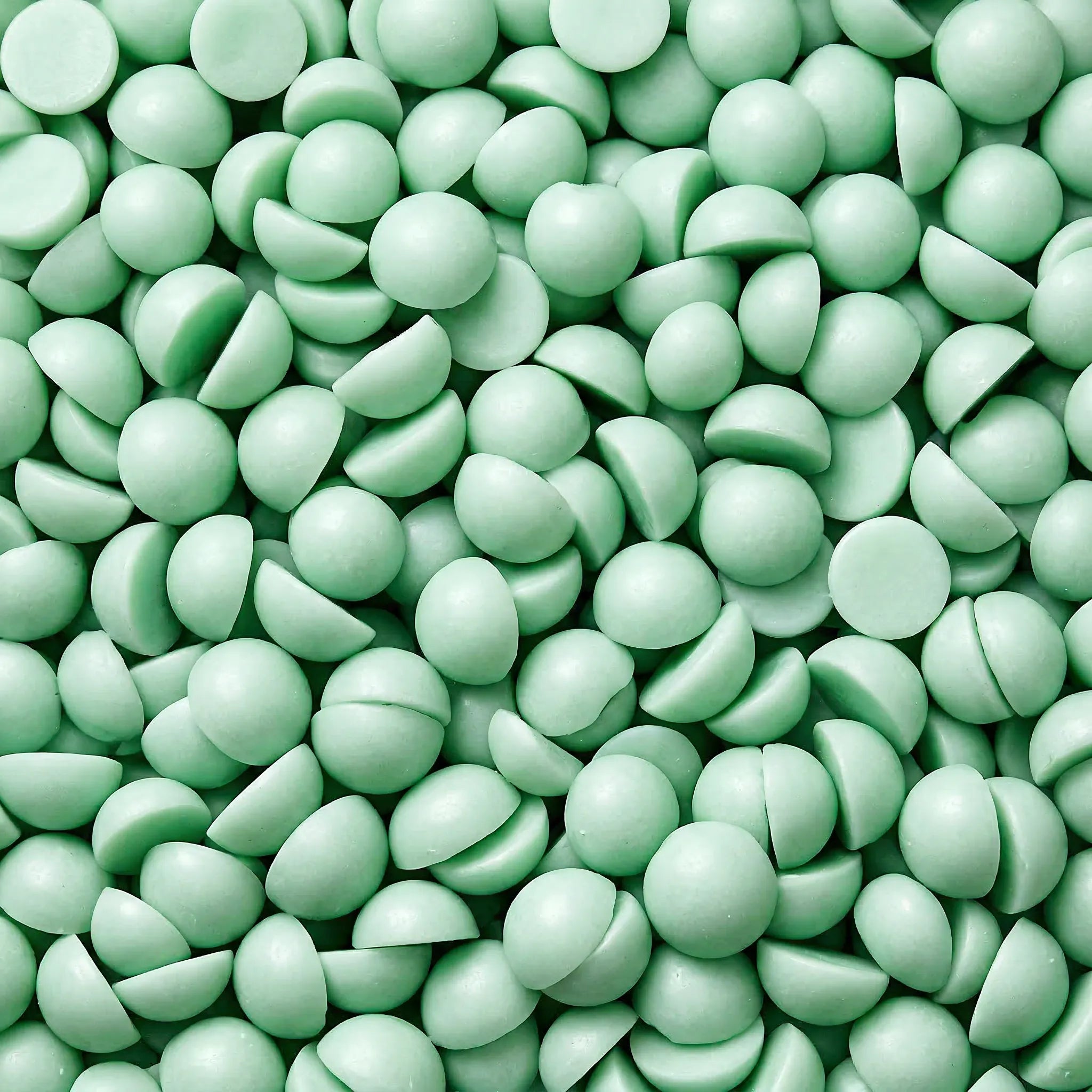 Nærbilde av små duftvokskuler i grønn farge. Tilhører duftvoksen "Forbudt på søndag" som har duft av nyklipt gress. Små halvkuler, håndlaget i norge.