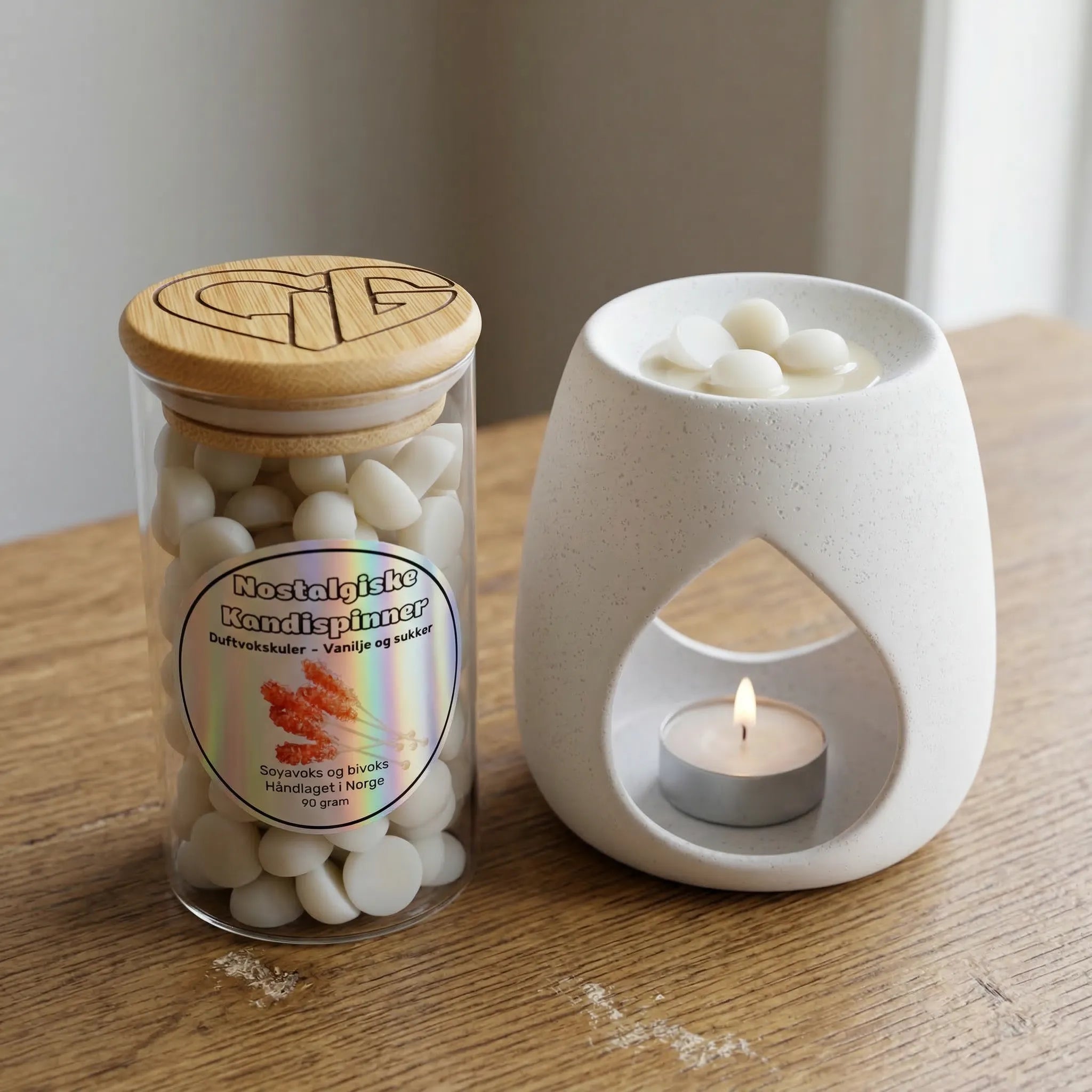 Duftvokskuler i glass med duft av kandispinner. En nostalgisk duft. Ved siden av glasset står en voksbrenner med et tent telys, som smelter noen kuler med duftvoks, og sprer den gode søte duften ut i rommet. Hvert glass inneholder 90g voks. Hver eneste duftvokskule er håndlaget i Norge.