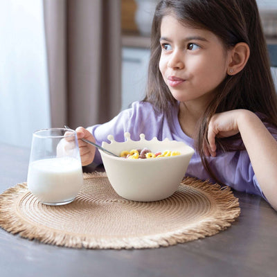 Jente som spiser frokostblanding av en designbolle, der melken ser ut til å sprute over kanten. Morsom og praktisk frokost skål som ikke kommer til å bli ødelagt da den er laget i silikon og tåler en støt. I tillegg er den morsom med melk som spruter. 