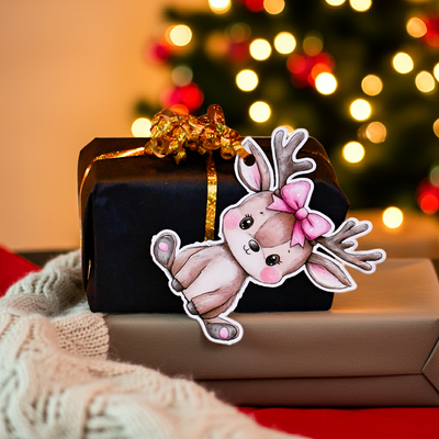 Til og fra lapp til julegavene. Her henger det lille reinsdyr barne med rosa sløyfe i håret på en julegave. Hun har hull i øret som båndet enkelt kan trees igjennom så gavelappen henger fint på julegaven uten å falle av. 