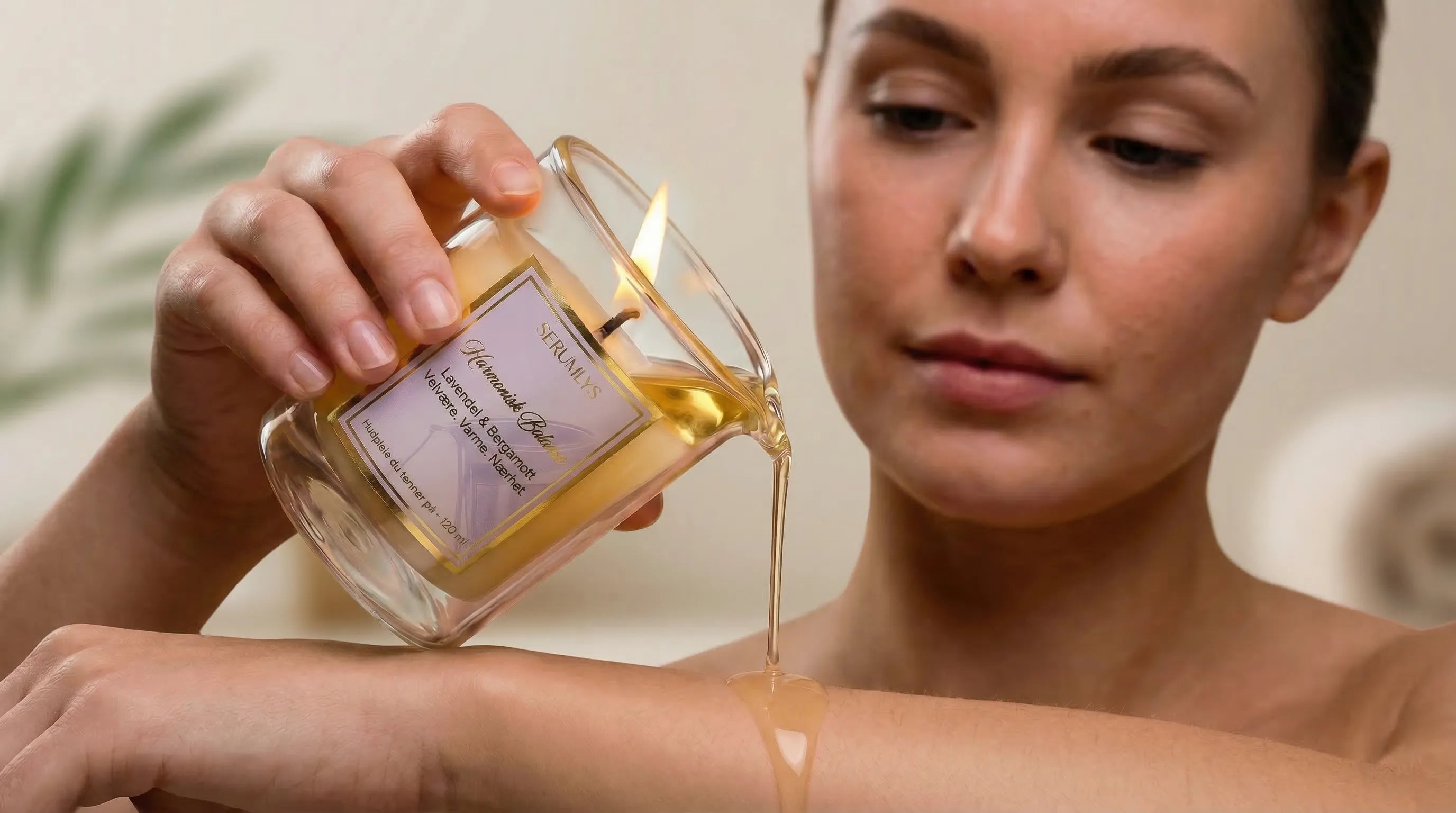 Tent serumlys som helles på armen. Naturlig hudpleie i form av et duftlys. Kvinnen holder varianten Harmonisk Balanse med duft av lavendel og bergamott. Håndlaget i norge med syv ulike planteoljer