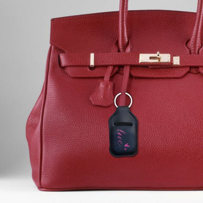 En nøkkelring i sort farge med rosa Love tekst og to rosa hjerter. Denne har plass til ørepropper. Nøkkelringen er festet på en rød veske. 