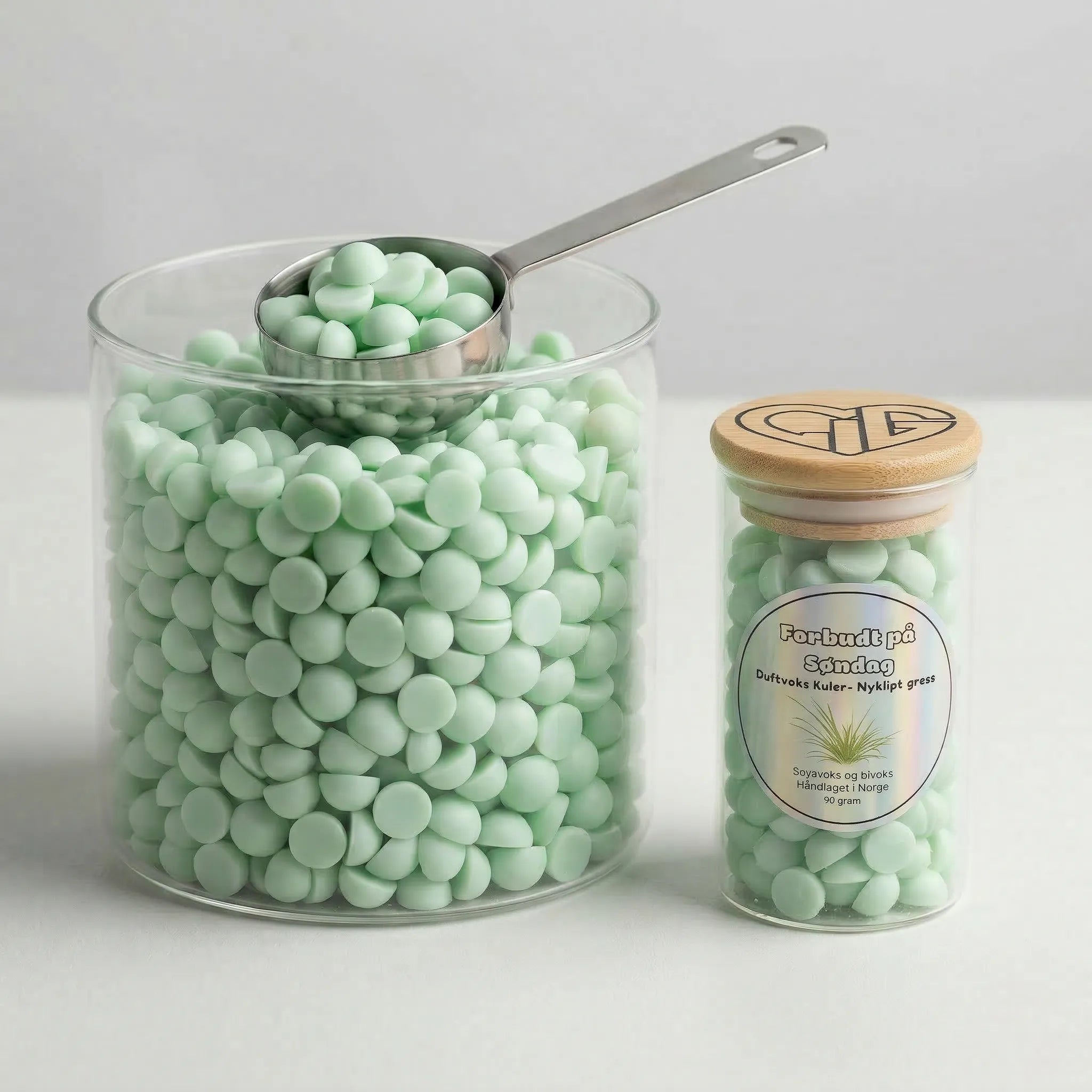 Forbudt på søndag duftvoks. I en stor beholder med glass ved siden av. Hvert glass rommer 90g voks. Voksen er laget av soyavoks og bivok. Duften av nyklipt gress.