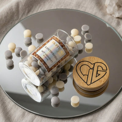 Små duftvokskuler i glass som ligger på et speil. Trelokk med Hjertelig AS sin logo ved siden av. Duftvoksen er laget av bivoks og soyaboks, og lukter kandispinner. Denne søte duften skal virke lindrende mot sårbarhet. Håndlaget i Norge.