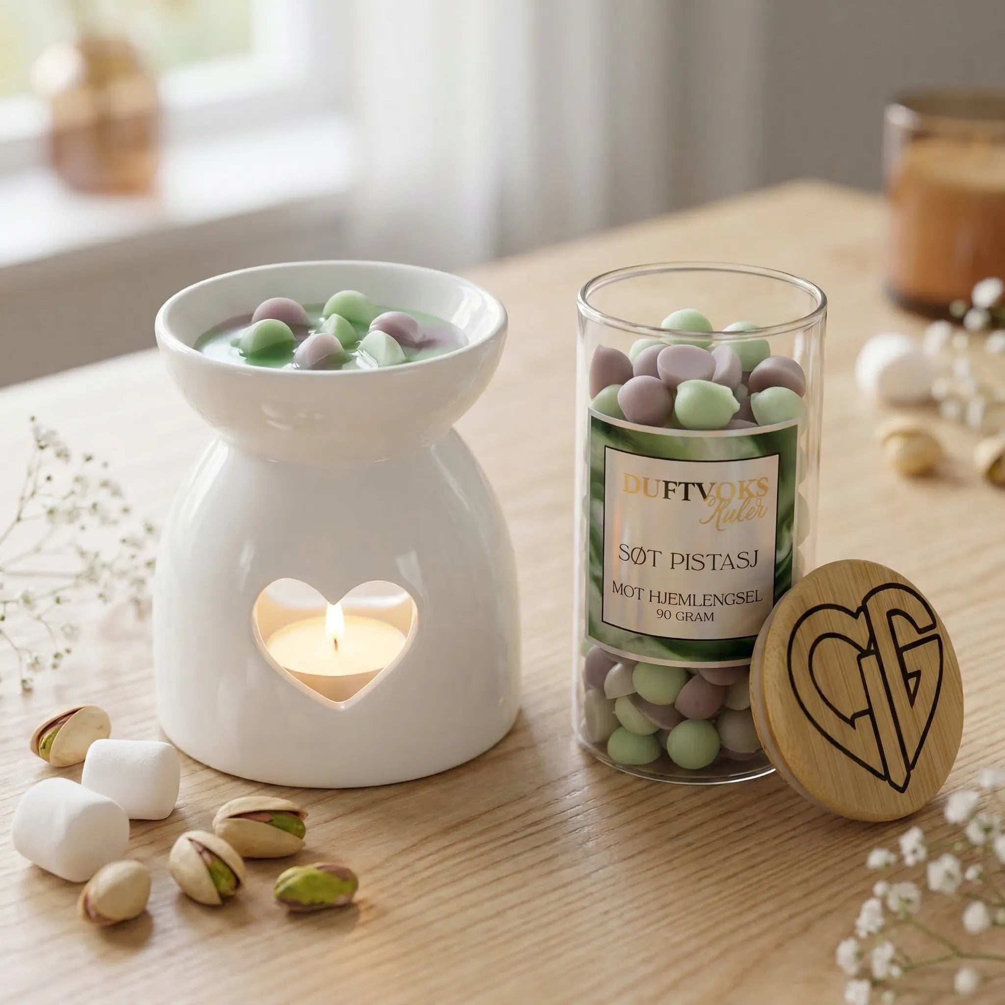 Duftvoks i glass. Noen duftvokskuler smelter i en duftbrenner. Duften av pistasjnøtter og marchmallows. En duft som skal lindre mot følelsen av hjemlengsel. Håndlaget i norge med bivoks og soyavoks.