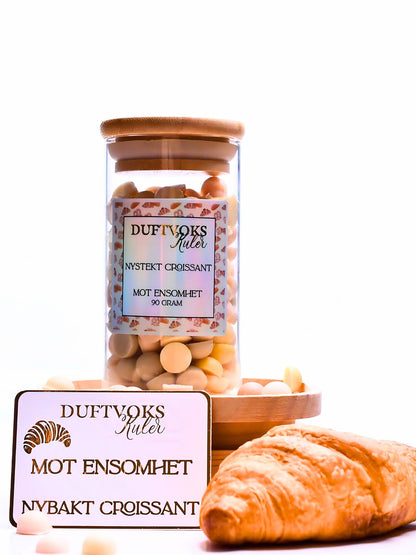 Duftvoks laget av soyavoks. På bilde ser du kortet du får med når man kjøper denne duftvoksen. På kortet står mot ensomhet, så er det vi har tenkt at denne duften kanskje kan hjelpe noen å komme igjennom i tunge perioder i livet. På siden ligger en Croissant som er duften på disse vokskulene. De lukter nydelig croissant. Følelsen av å være på et bakeri i Frankrike. Herlige dufter av nystekt bakst.