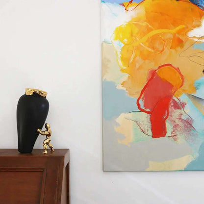 En sort vase med gullkant som står på et brunt bord. Ved siden av bordet ser man et maleri på veggen. Dette er en håndlaget vase fra nederland. Et kunstverk og nydelig dekorasjon både med eller uten blomster.